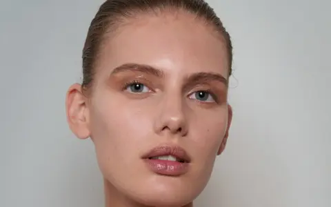 Delikatna skóra modelki, nawilżona kwasem poliglutaminowym, z subtelnym makijażem oczu i błyszczącymi ustami.