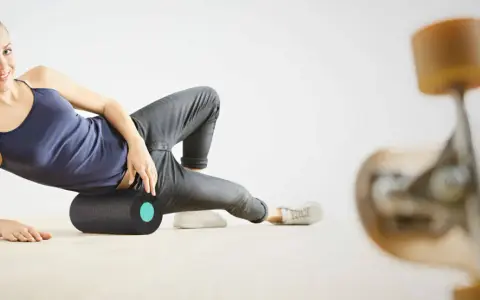 Frau rollt mit einer Faszienrolle über ihr Knie, um Muskelverspannungen zu lösen. Ein Skateboard ist im Vordergrund unscharf zu sehen.