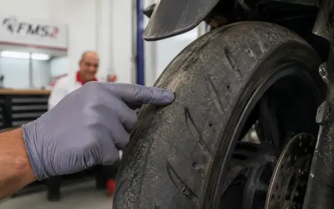 Mano guantata indica il battistrada minimo di una moto, mostrando l'usura.