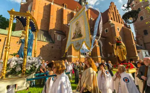 Prozession mit Marienstatue und Fahne vor einer Kirche. Menschen in weißen Gewändern, ein Festtag in Polen.