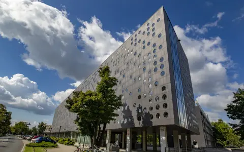 Nowoczesny budynek SWPS Wrocław z okrągłymi oknami, pod błękitnym niebem z chmurami.
