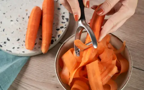 Des carottes épluchées tombent en rubans dans un bol. Une astuce pour comment conserver les carottes : les préparer ainsi pour une cuisson rapide.