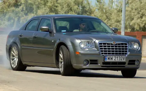 Szary Chrysler 300S z dymiącymi oponami, kierowca za kierownicą, na drodze.