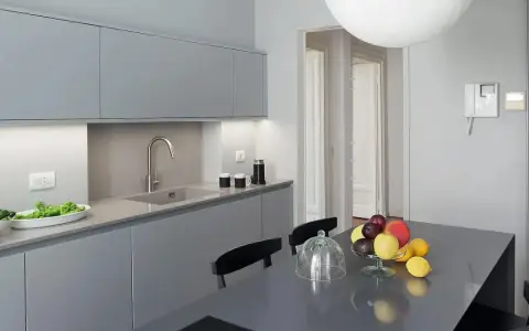 Cucina moderna con pensili e basi grigie. Il colore pareti neutro esalta la pulizia delle linee. Tavolo con frutta fresca.