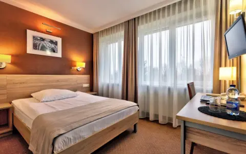 Przytulny pokój hotelowy w Białymstoku z wygodnym łóżkiem, biurkiem i telewizorem.