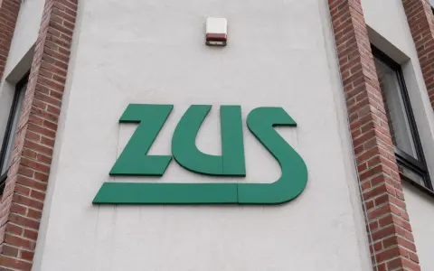 Zielone logo ZUS na białej ścianie budynku z ceglanymi elementami.