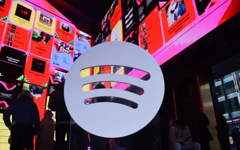 Duże logo Spotify na tle ekranów z podsumowaniami słuchania, w tym informacją o najpopularniejszym artyście na Spotify.