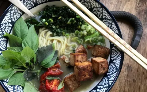 En skål med vegetarisk ramen med nudlar, tofu, grönsaker och basilika.