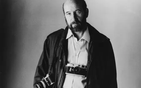 Ritratto di Gianni Berengo Gardin, fotografo con due macchine fotografiche al collo, sguardo intenso.