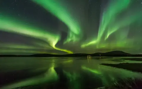 Grönt norrsken dansar över en frusen sjö i Finland. Stjärnor lyser på himlen och speglar sig i vattnet.