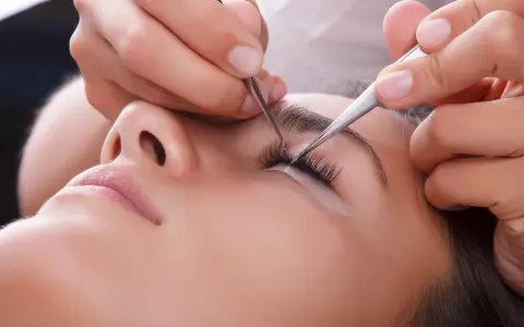 Pose de cils : quelle pince à épiler choisir pour un résultat parfait. Une esthéticienne applique des extensions de cils avec précision.