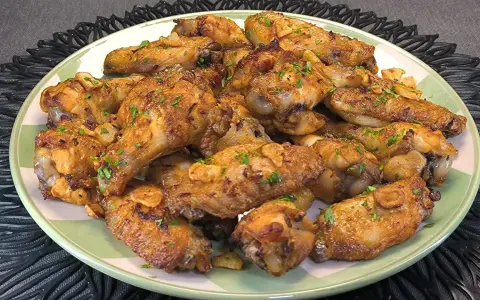 Alitas de pollo doradas con ajo y perejil en un plato verde.