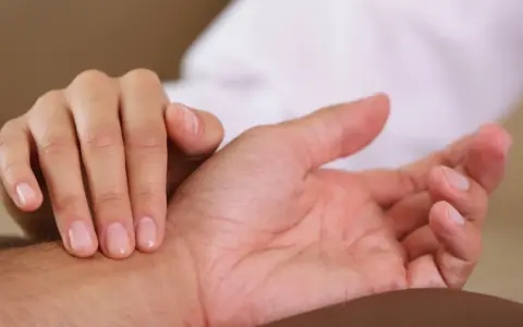 Dłoń pielęgniarki bada tętno na nadgarstku pacjenta, sprawdzając prawidłowe tętno.