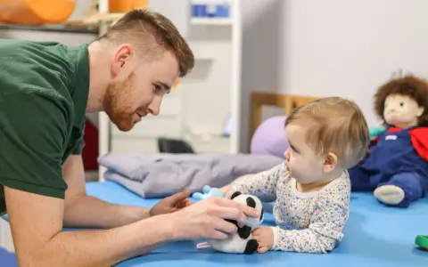 Osteopata dla dzieci delikatnie bawi się z niemowlęciem pluszową pandą, wspierając jego rozwój.