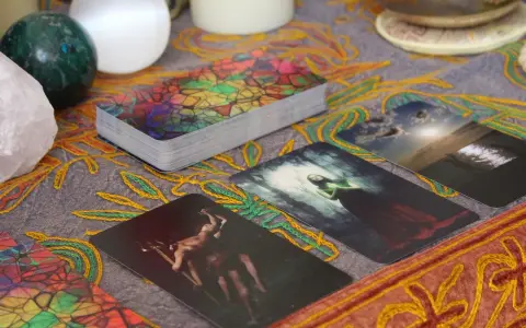 Tarot dzienny ryby: karty z mistycznymi obrazami, kryształ, kule i ozdobny obrus tworzą atmosferę wróżenia.