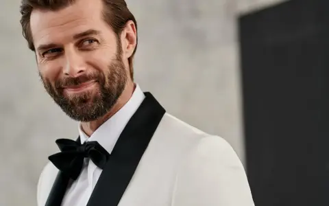 Elegancki mężczyzna w białej marynarce z czarnymi klapami i czarną muszką. Jego męski strój wieczorowy podkreśla jego urok.