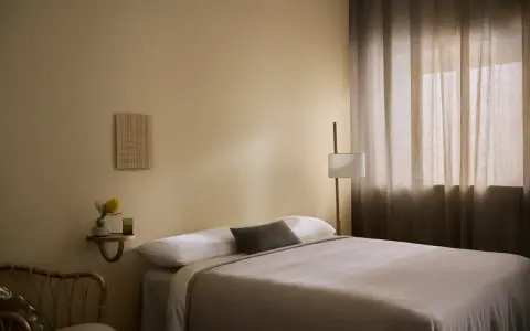 Ett lugnt sovrum med beige väggar, en bekväm säng och en golvlampa. Perfekt för att måla sovrum i en avkopplande stil.