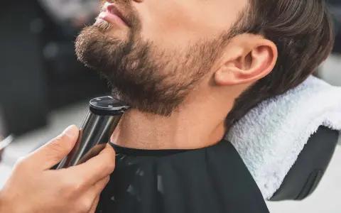 Barbero perfilando barba con recortadora, creando diseños de barba modernos.
