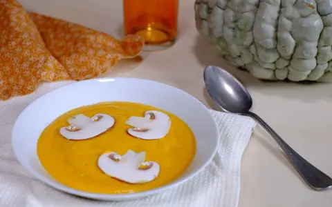 Soupe de courge orange avec des champignons, une serviette orange et une courge entière, évoquant une ambiance de Marina di Chioggia.