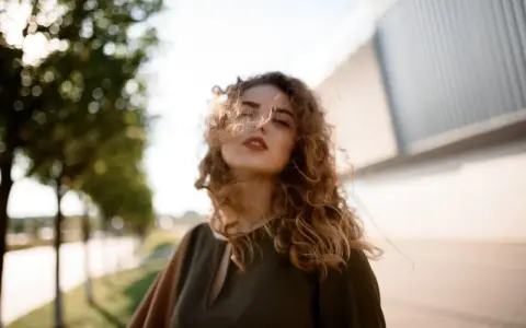 Kobieta z burzą kręconych włosów, wiatr rozwiewa jej kosmyki. Idealny przykład, jak utrwalić loki, by wyglądały naturalnie i pięknie.