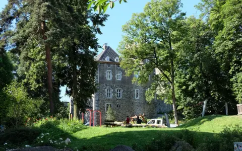 Ein sonniger Tag im Frankenberger Park. Kinder spielen auf einem Spielplatz vor einem alten Gemäuer, umgeben von üppigem Grün.