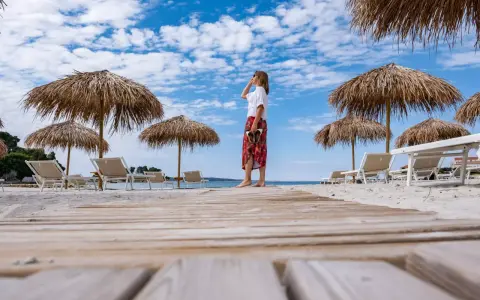 Kobieta na plaży, pod słomianymi parasolami, podziwia widok. To idealne miejsce na wyspie Rab, atrakcje czekają!