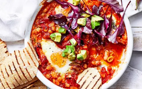 Herzhaftes Gericht mit pochierten Eiern in Tomatensoße, Bohnen, Avocado und Rotkohl. Perfekt für gesunde Rezepte Abendessen. Dazu geröstetes Fladenbrot.