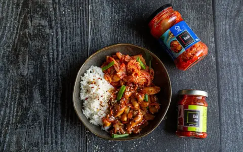 Miseczka z ryżem i kurczakiem po koreańsku, z dodatkiem kimchi i sosu chili.