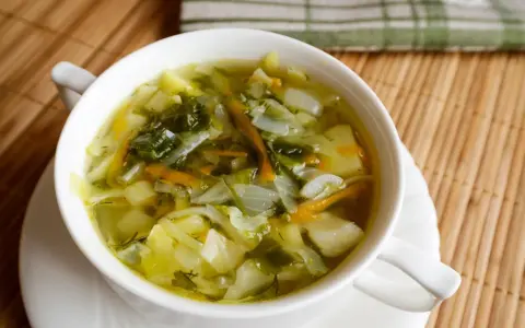 Aromaticzny kapuśniak z młodej kapusty, pełen warzyw i ziół, podany w białej miseczce.