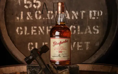 Butelka Glenfarclas 10 Year Old, jedna z 10 najlepszych whisky, na tle beczki. Młotek sugeruje rzemiosło.