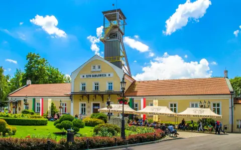 Wieliczka atrakcje: Szyb Daniłowicza, żółte budynki kopalni, zielony ogród i ludzie odpoczywający pod namiotami.