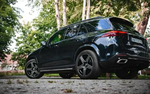 Ciemny Mercedes GLE 350 zaparkowany na kamienistej drodze, otoczony zielenią drzew.