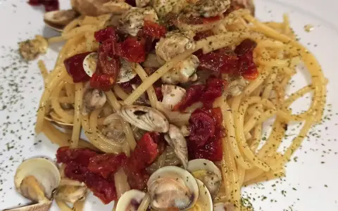 Spaghetti con lupini e pomodorini secchi, un piatto di mare saporito e profumato, guarnito con prezzemolo tritato.