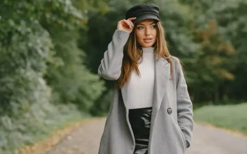 Elegancka kobieta w czapce i szarym płaszczu, prezentująca stylowe stylizacje z szarym płaszczem na tle jesiennego parku.