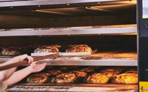 Bäcker lässt den **backofen spalt offen lassen beim backen** für knuspriges Brot. Mehrere Brote auf Regalen im Ofen.