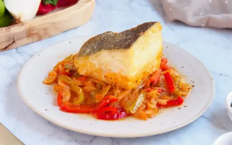Un delicioso bacalao encebollado reposa sobre una cama de pimientos y cebolla.