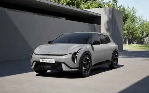 Nowoczesny, jasnoszary Kia EV4 GT-Line stoi na podjeździe przed minimalistycznym budynkiem.