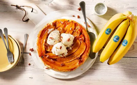 Tarte banane caramel beurre salé, garnie de boules de glace à la vanille et de noix de pécan. Des bananes Chiquita sont à côté.