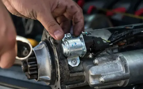 Mechanik naprawia rozrusznik w aucie, przykręcając element.