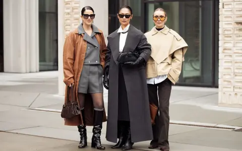 Drei Frauen präsentieren stilvolle Outfits im layering look: brauner Mantel über grauem Anzug, langer grauer Mantel und beiger Kurzmantel über weißem Hemd.