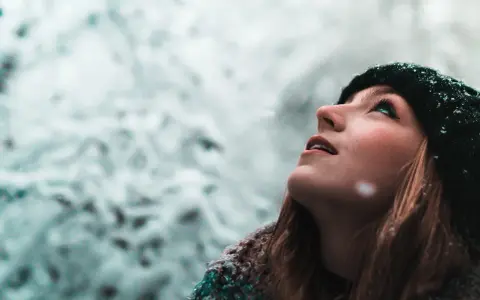 Junge Frau blickt in den Schnee, ihre Wangen gerötet, ein Zeichen von trockene Haut im Winter.