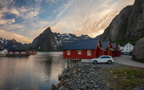 Röda fiskestugor vid vattnet i Lofoten, perfekt boende för en stuga-semester med dramatiska berg i bakgrunden.
