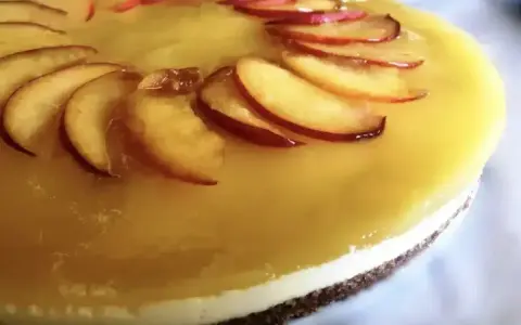Cheesecake alla pesca con fette di pesca fresca disposte a raggiera sulla glassa gialla.