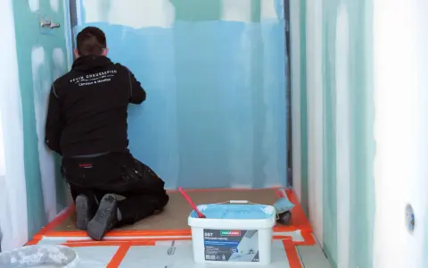 Un carreleur applique une protection étanche avant la pose carrelage dans une douche.
