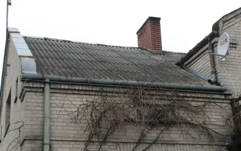 Dach pokryty eternitem, który zawiera azbest. Co to za materiał? Stary, szary eternit na dachu domu, z kominem i anteną satelitarną.
