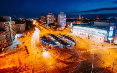 Widok z lotu ptaka na nocne miasto z długimi smugami świateł samochodowych i tramwajowych.