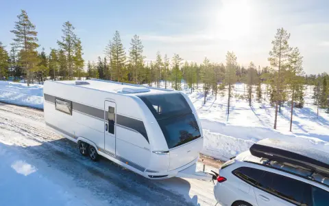 Vit husvagn dras av bil genom snöig skog. Den bästa husvagnen för äventyr nära Haparanda.