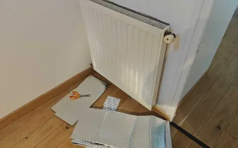 Un radiateur derrière une porte, prêt à être isolé avec des feuilles argentées et des ciseaux.