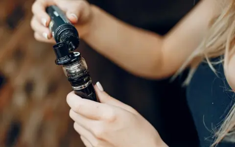 Manos rellenando un vaporizador con líquido de nicotina salina.
