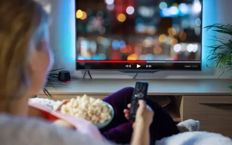 Persona relajada viendo una serie en francés en la televisión, con palomitas y mando a distancia.